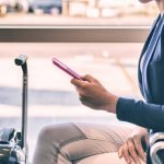 Plane passenger woman waiting for flight departure texting sms message on mobile phone at lounge airport. Businesspeople travel lifestyle panoramic banner.