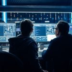 Two Professional IT Programers Discussing Blockchain Data Network Architecture Design and Development Shown on Desktop Computer Display. Working Data Center Technical Department with Server Racks